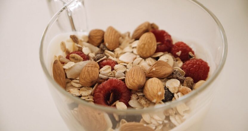 A glass bowl filled with yogurt, granola, almonds, raspberries, and other healthy ingredients